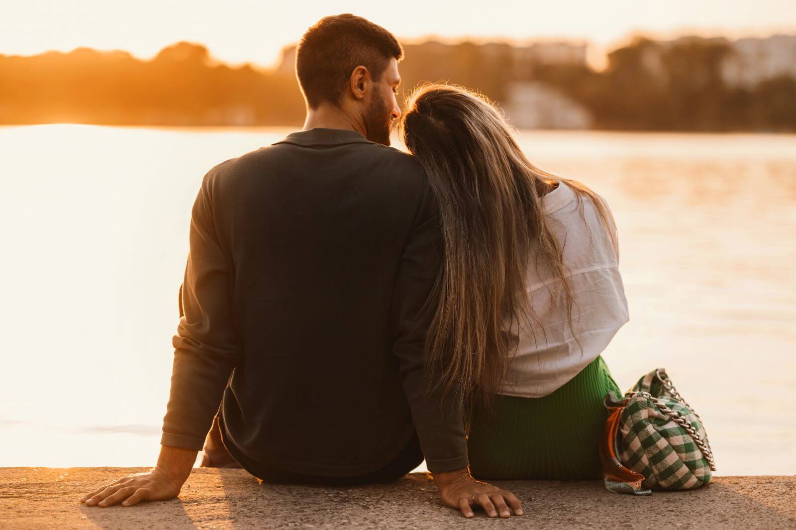 Couple sitting together by the lake at sunset, sharing a moment of intimacy and relaxation.