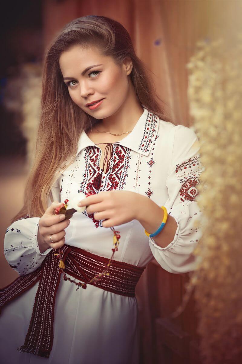 Young Ukrainian woman in traditional embroidered blouse with long hair, softly smiling at the camera.