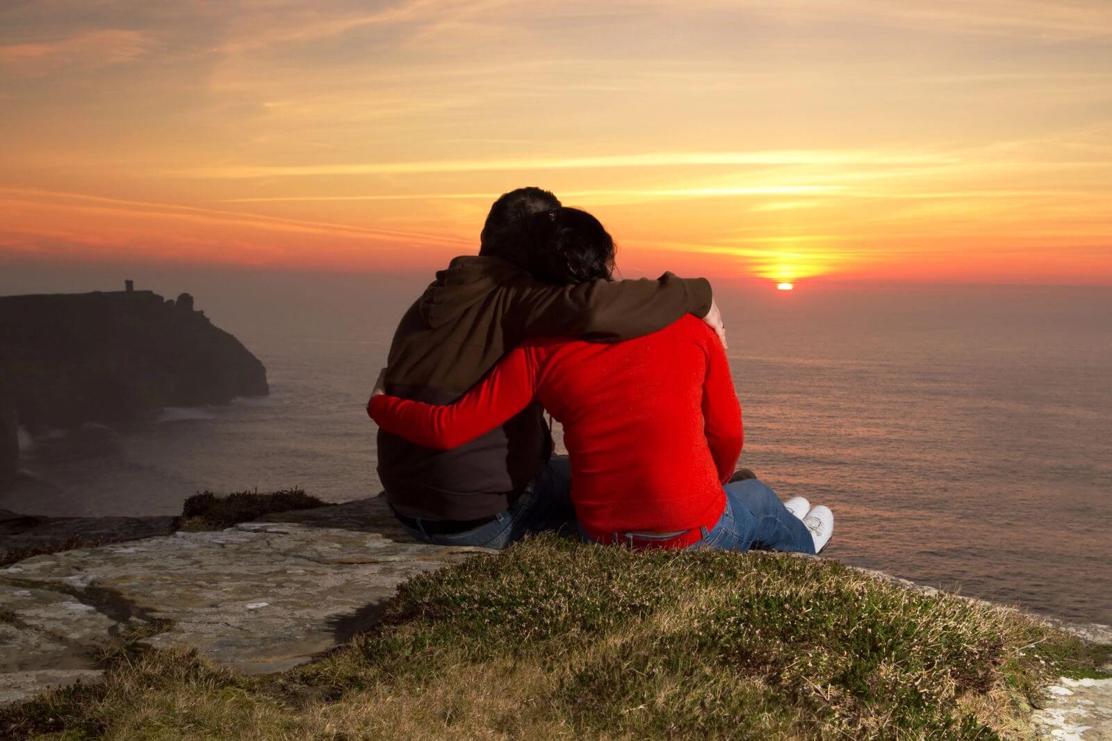 Couple sitting on a cliffside watching the sunset over the sea