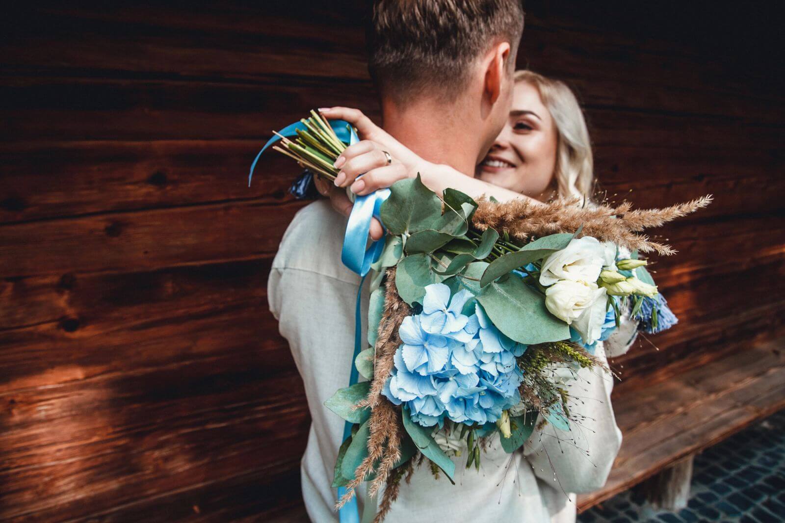Bride embracing groom while holding a bouquet with blue hydrangeas and white flowers.